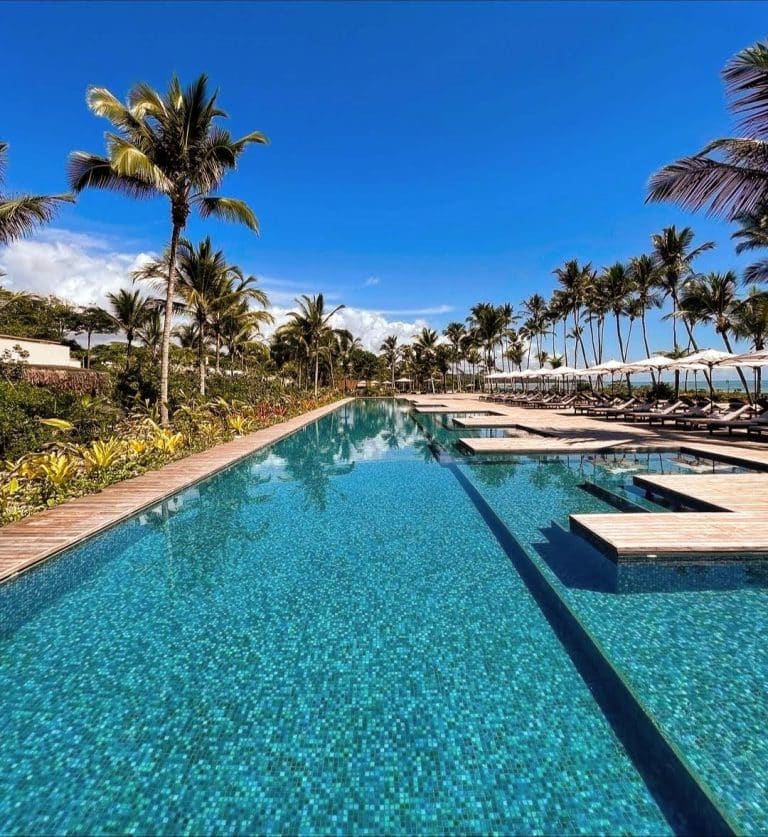 Piscina de borda infinita cercada por palmeiras no Hotel Fasano Trancoso em um dia ensolarado.