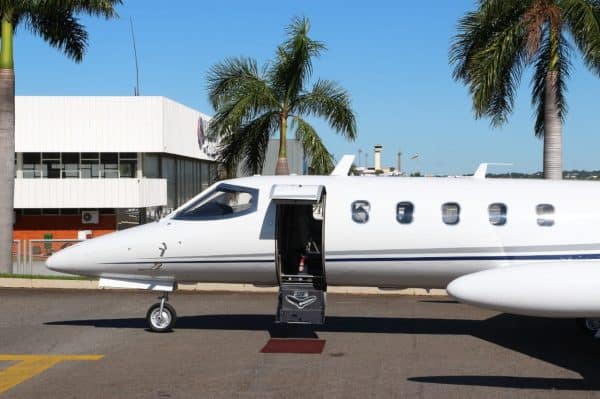 Jato executivo branco estacionado na pista de um aeroporto, com a porta aberta, preparado para embarque.