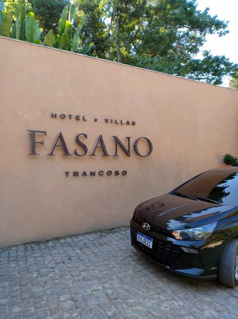 Carro preto estacionado em frente à fachada do Hotel Fasano Trancoso, em meio à natureza exuberante.